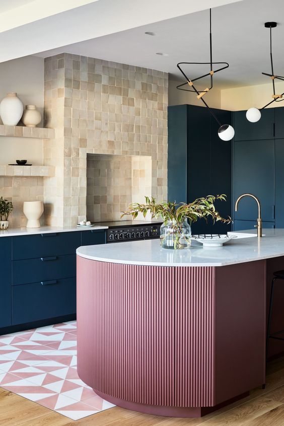 a bright kitchen with navy cabinets, a tan and beige Zellige tile backsplash and wall, a pink kitchen island and lamps