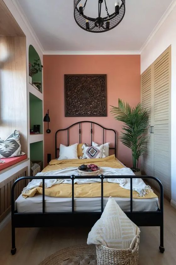 a bright narrow bedroom with open storage compartments, a wardrobe, a forged bed with bright bedding, a potted plant and a windowsill daybed