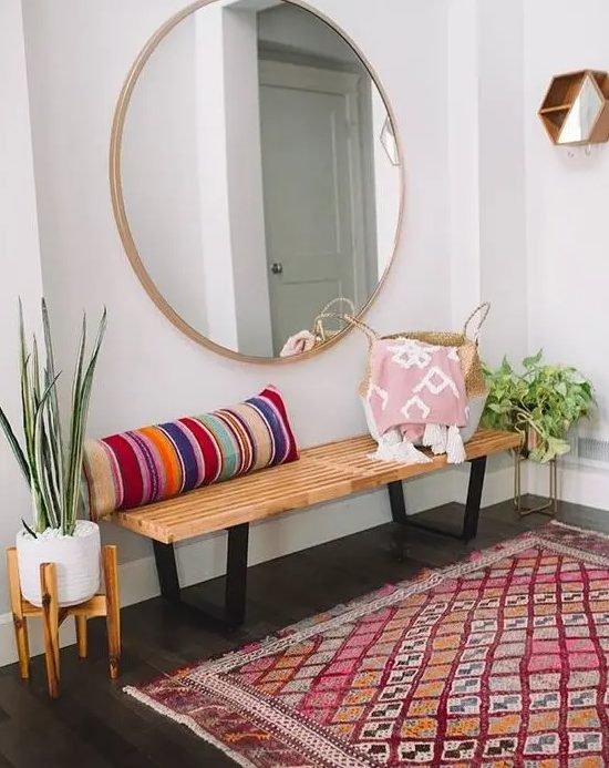 a-colorful-boho-entryway-with-a-wooden-bench-a-striped-pillow-a-round-mirror-a-bright-rug-and-potted-plants.jpg