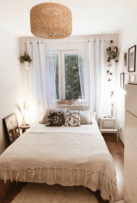 a cozy narrow bedroom with a bed and neutral bedding, mismatching nightstands, a dresser and some potted plants