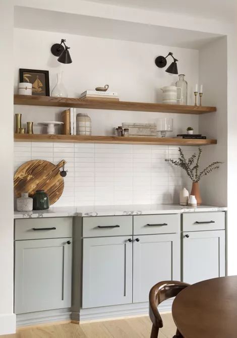 a dove grey kitchen with white marble countertops, stained shelves, a white stacked tile backsplash and black lamps