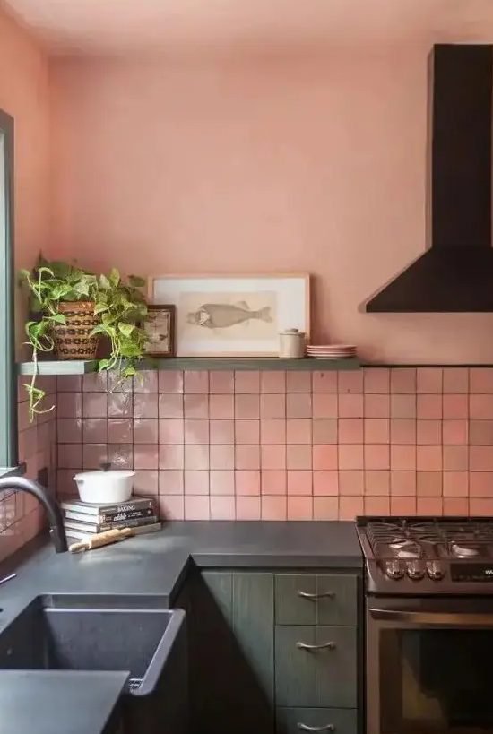 a gorgeous kitchen with pink zellige tiles, green cabinetry, black appliances and fixtures, a shelf with some art and a potted plant