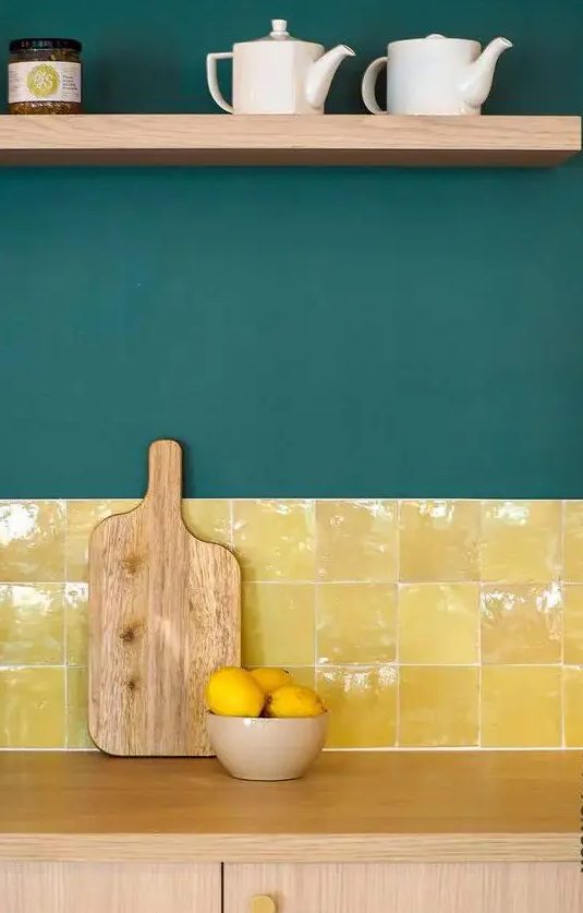 a light-stained kitchen with dark green walls and a bold and shiny yellow tile backsplash plus an open shelf is a lovely idea