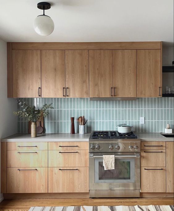 a light-stained kitchen with white countertops and mint blue stacked tiles, white countertops and black handles