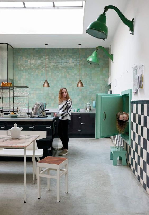 a lovely retro kitchen with black cabinets, a bold green Zellige tile wall, bold green touches and neutral dining furniture