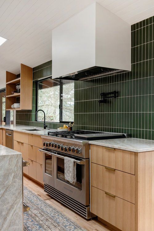 a mid-century modern kitchen with stained cabinets, a green stacked tile backsplash and black fixtures