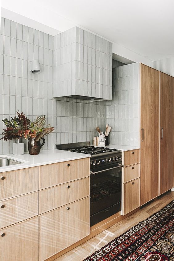 a mid-century modern kitchen with stained cabinets, grey stacked tiles and white countertops