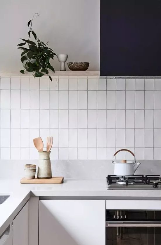 a minimalist grey kitchen with a navy hood, wooden shelves and a white stacked tile backsplash