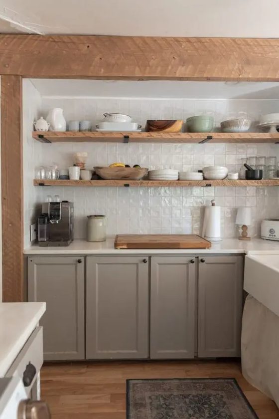 a modern farmhouse kitchen with grey shaker cabinets, white stone countertops, a white zellige tile backsplash and open shelves