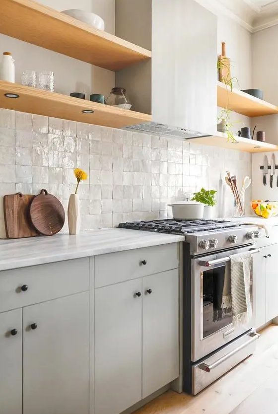 a modern grey kitchen with a zellige tile backsplash, open shelves, a hood and black knobs for a catchy detail