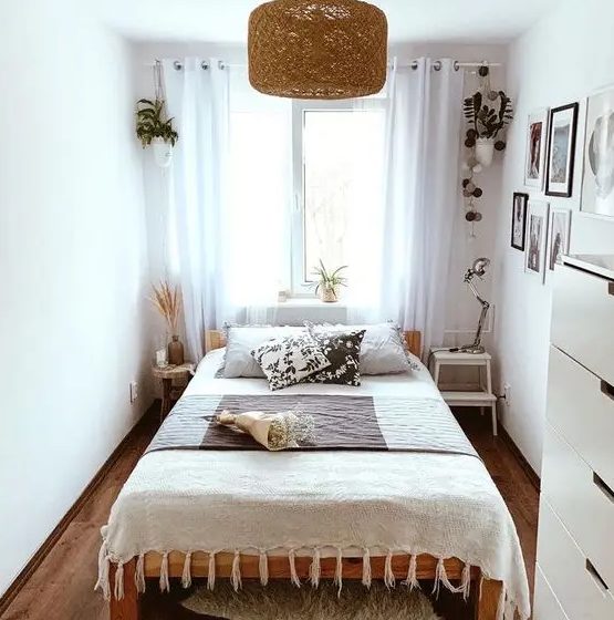 a modern narrow bedroom with a bed with printed bedding, mismatching nightstands, potted plants, a gallery wall and a dresser
