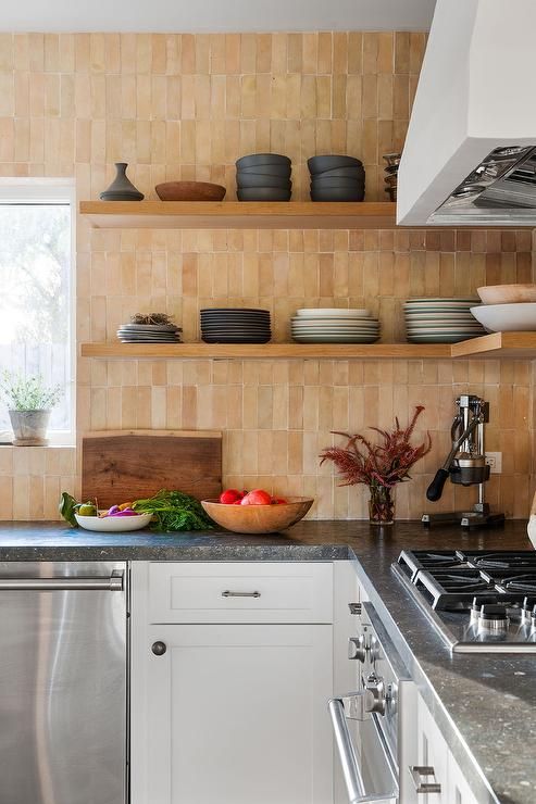 a modern white kitchen with shaker cabinets, grey countertops, a Zellige stacked tile backsplash and stained shelves
