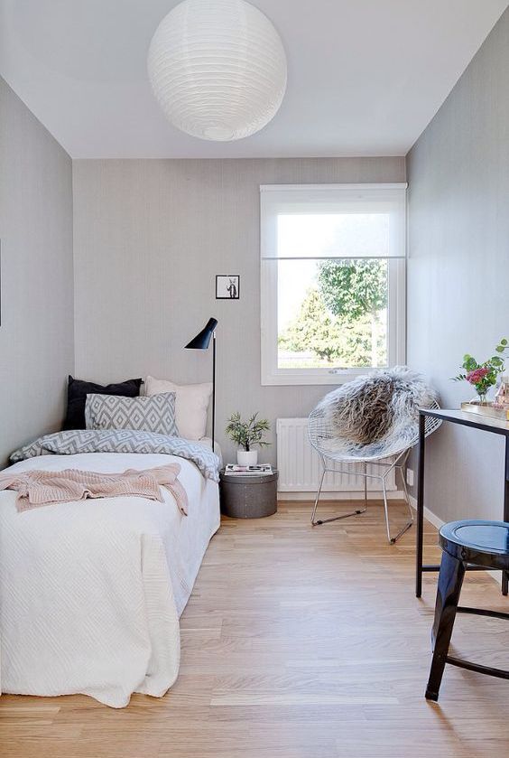 a narrow bedroom in dove grey, with a bed and printed bedding, a metal chair, a desk, a stool and a floor lamp