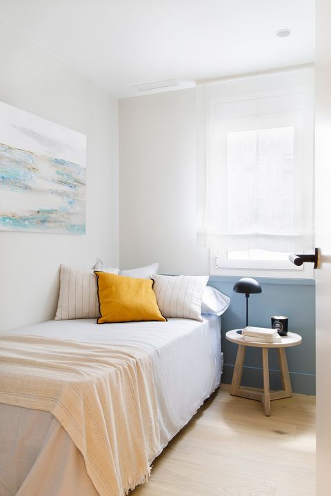 a narrow bedroom with a single bed, neutral bedding, a nightstand with a lamp, an artwork is a lovely space