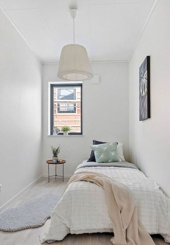a narrow guest bedroom with a single bed and neutral bedding, a nightstand, some art and a pendant lamp