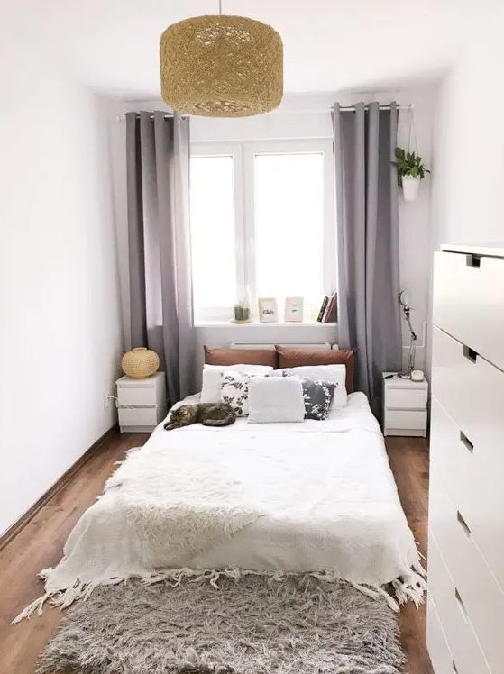 a neutral narrow bedroom with a bed, matching nightstands, a fluffy rug, a pendant lamp and a dresser