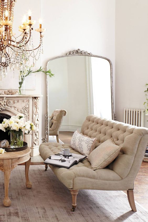 a-refined-French-living-room-with-a-carved-fireplace-a-large-floor-mirror-a-neutral-loveseat-a-table-with-blooms-and-a-chic-chandelier.jpg