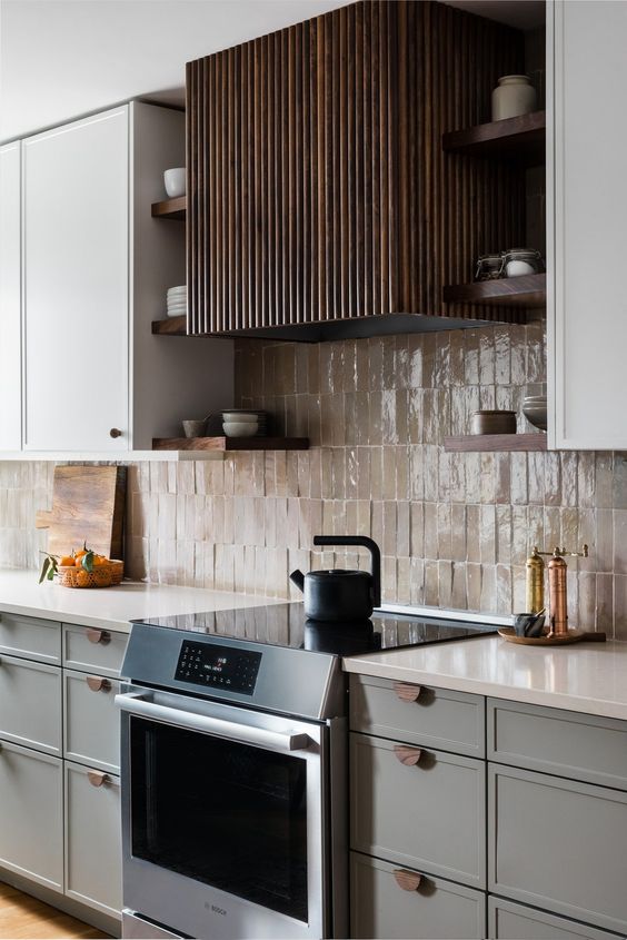 a refined grey and white kitchen with white countertops, a tan Zellige tile backsplash and a dark fluted hood is chic