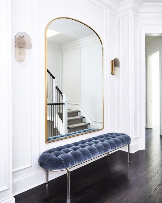 a-refined-minimalist-entryway-with-a-pretty-arched-mirror-in-a-gilded-frame-a-blue-uphalstered-bench-and-sconces.jpg