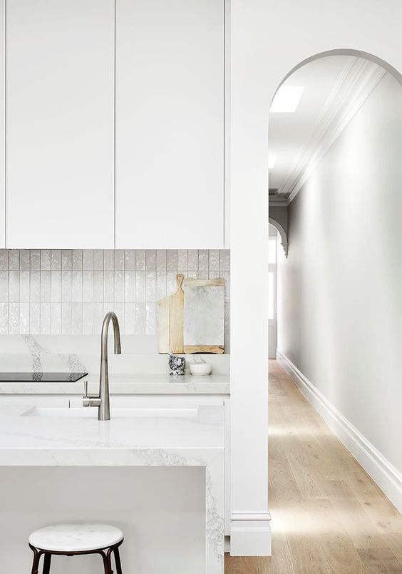 a refined white kitchen with sleek cabinets, a white stacked tile backsplash, a kitchen island and stainless steel fixutres