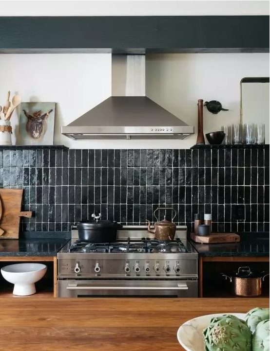 a rich stained wooden kitchen with black stone countertops, a black skinny tile backsplash and stainless steel appliances