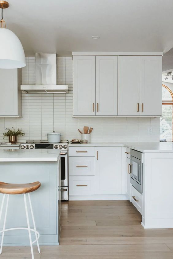 a serene white kitchen with a stacked tile backsplash, shaker cabinets, white countertops and wooden stools