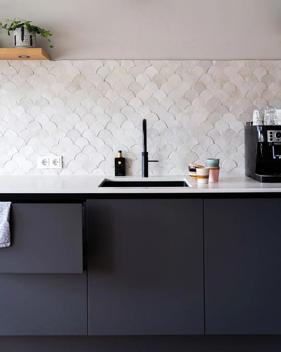 a sleek matte black kitchen with a pearly scallop tile backsplash, a white stone countertop and open shelves