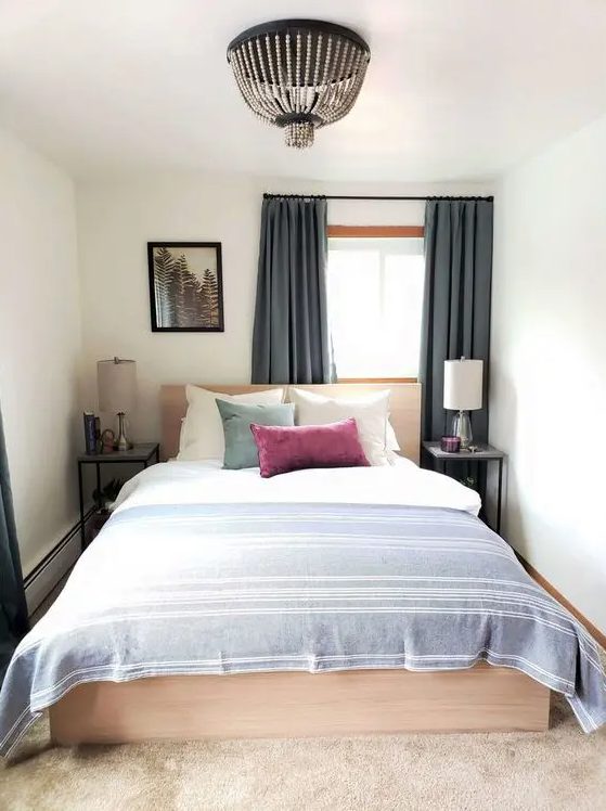 a small and narrow bedroom with a light-stained bed and neutral bedding, nightstands with lamps and a beaded chandelier