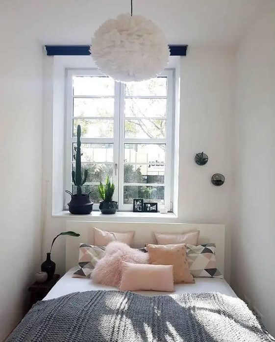 a small and narrow bedroom with a white bed, pink and printed bedding, a single nightstand and some potted plants
