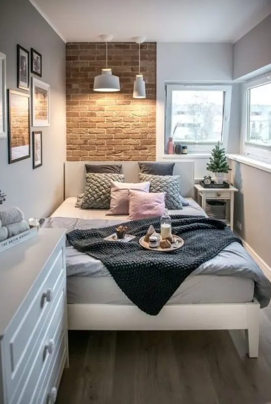 a small contemporary bedroom with a brick wall, a white bed and dresser, pendant lamps and catchy bedding