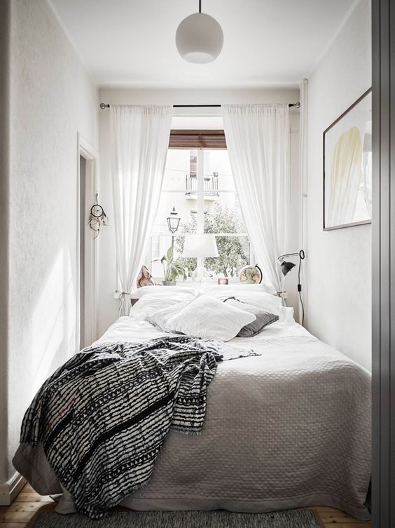 a tiny narrow bedroom with a bed and neutral bedding, a wall lamp and an artwork for cozy sleeping here