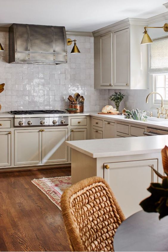 a vintage-inspired kitchen with tan cabinets, white countertops, a white Zellige tile backsplash and brass lamps