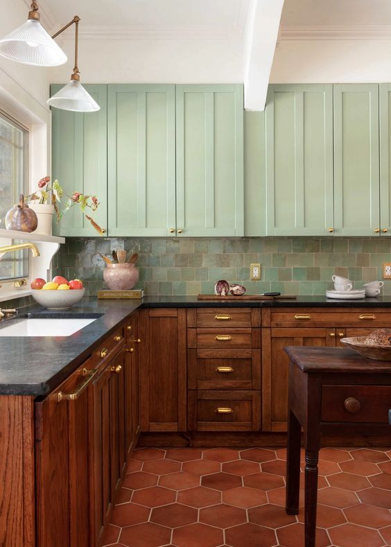a vintage kitchen with mint green and stained cabinets, a green Zellige tile backsplash and black countertops plus a stained kitchen island