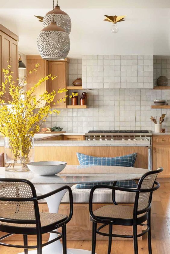 a welcoming kitchen with light-stained cabinetry, a white Zellige tile bacskplash, chic dining furniture