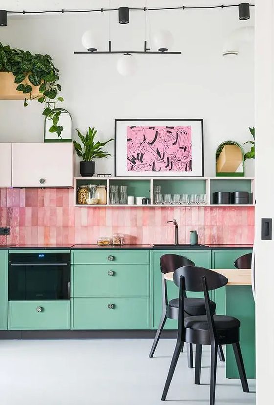 a whimsical kitchen with green cabinets and blush upper ones, a bold pink stacked tile backsplash and touches of black