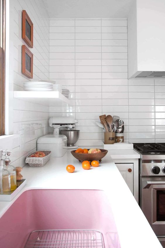 a white kitchen with a stacked tile backsplash, a white hood, open shelving and a pink sink is a cool and cute space