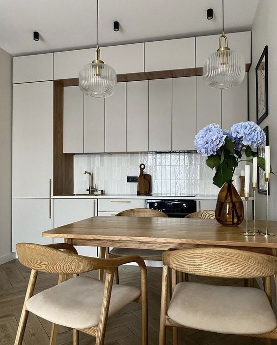 a white kitchen with several rows of cabinets, a white stacked tile backsplash and elegant dining furniture