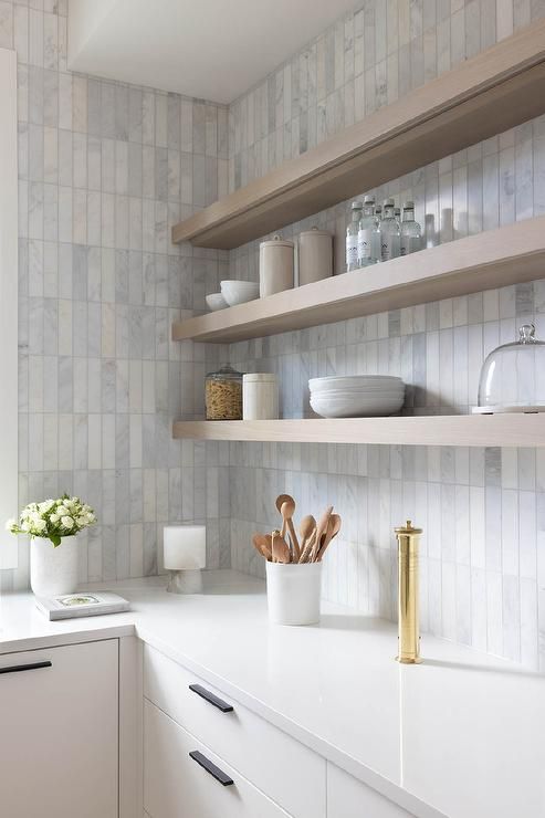 a white kitchen with stained shelves, white countertops and a marble stacked tile backsplash is a lovely and chic space