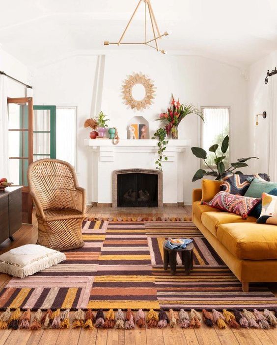 a-boho-living-room-with-a-colorful-striped-rug-a-yellow-sofa-with-printed-pillows-rattan-chair-a-fireplace-with-some-pretty-decor.jpg