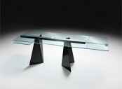 a modern dining table with a blue glass tabletop and black triangle legs and a construction that holds the tabletop is a catchy and architectural idea