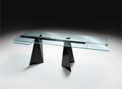 a modern dining table with a blue glass tabletop and black triangle legs and a construction that holds the tabletop is a catchy and architectural idea