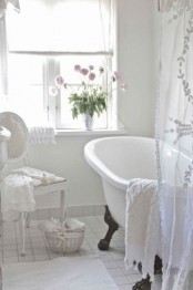 a white Provence bathroom with tiles on the floor, a clawfoot bathtub, a shabby chic chair, lace curtains and blooms