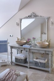 a neutral bathroom with a refined grey open vanity, bowl sinks and vintage faucets, a large mirror in a refined vintage frame plus various pastel towels