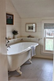 a neutral bathroom clad with wooden planks, with a chic vintage clawfoot bathtub, an open shelf and neutral and printed textiles