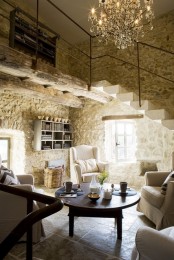 an inviting Provence living room with stone walls, a crystal chandelier, neutral furniture and a basket plus a low round table