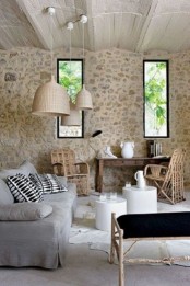 a rustic Provence living room with stone walls, neutral furniture, a low table and rattan chairs plus pendant lamps over the space