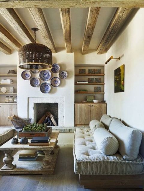 a stylish Provence living room with a fireplace, wooden beams, eclectic furniture, a rattan lamp and a low table