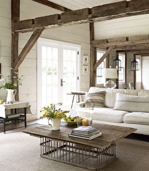 a lovely and welcoming Provence living room done in neutrals, with wooden beams, a wooden table, upholstered furniture and blooms