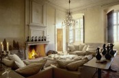 a neutral Provence living room with a refined fireplace, neutral furniture, a crystal chandelier and a coffee table with jugs