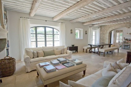 a neutral Provence living room with wooden beams, a fireplace, refined furniture, a low coffee table and a dining zone